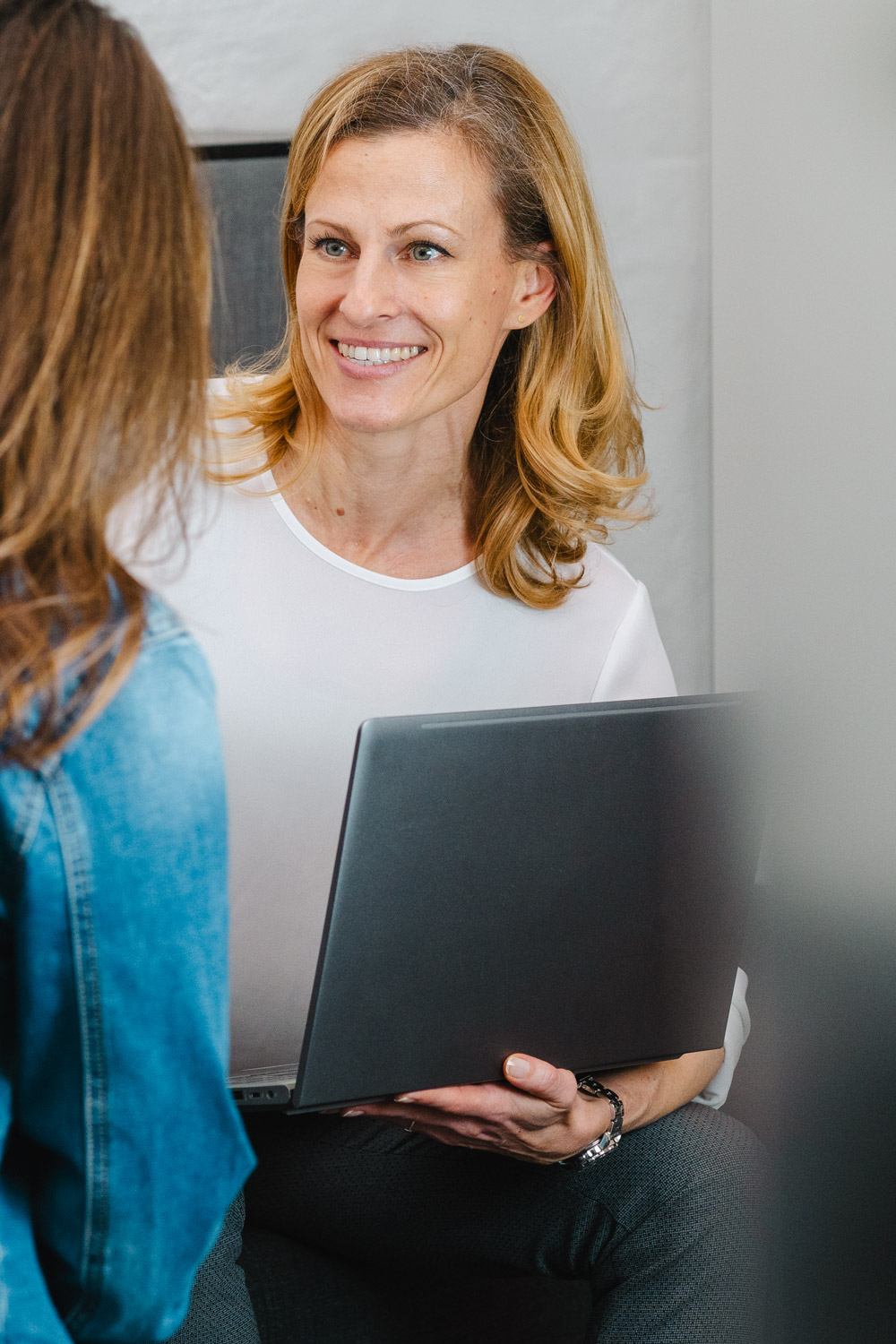 Sigrid Blodau, Marketing und Kommunikation bei re-sult, hält einen Laptop und spricht mit einer Kollegin.